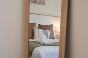 Ein ordentlich bezogenes Bett mit Kissen und Decke, eine Nachttischlampe und ein an der Wand befestigter Bilderrahmen.