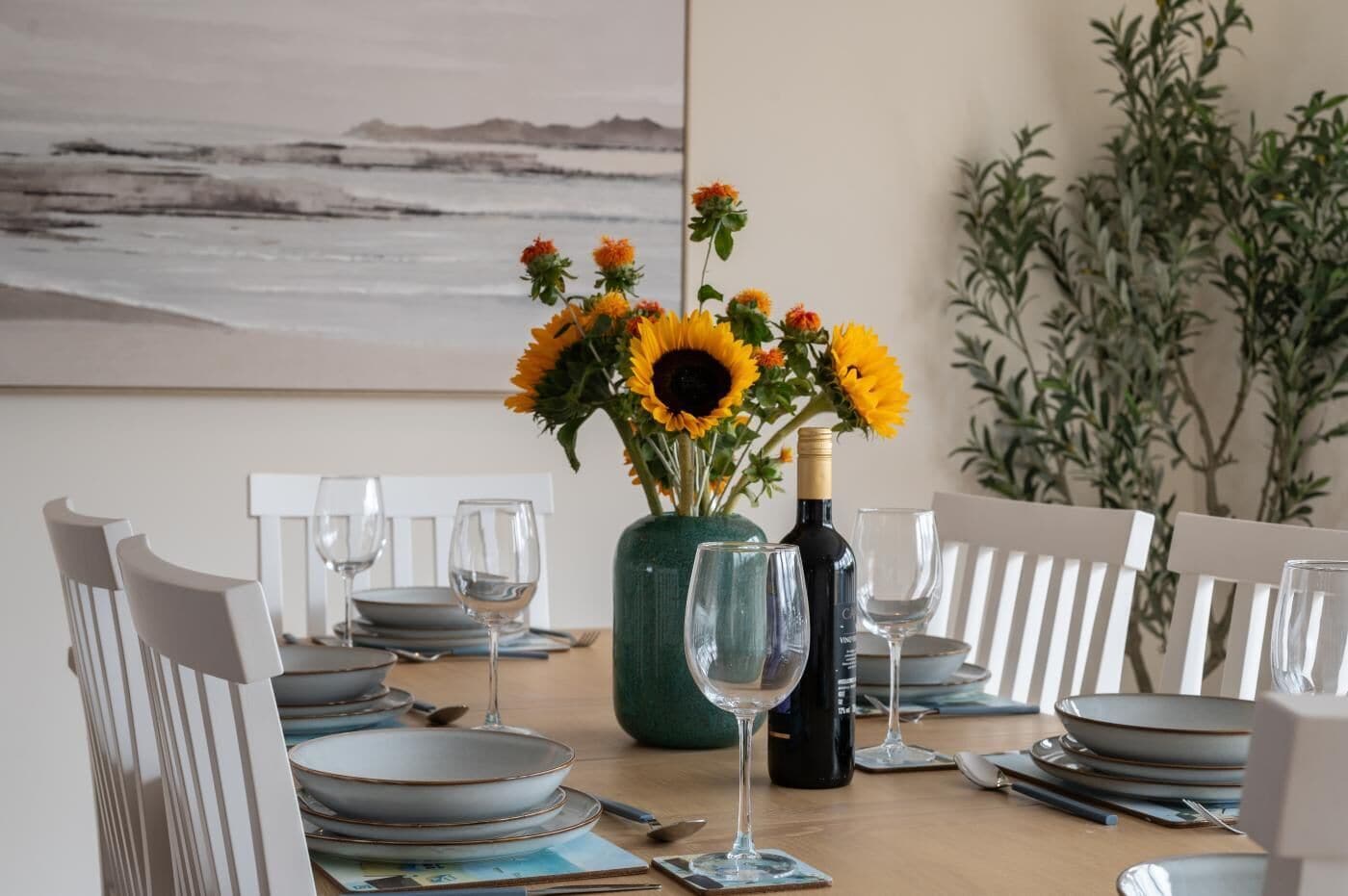 A dining table set with plates, glasses, and a vase of sunflowers.