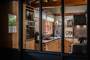 A compact kitchen with wooden cabinetry, a built-in oven, a sink, and a microwave. - Maison La Gravière - Five Bedroom Chalet, Sleeps 14 (La Salle-les-Alpes)