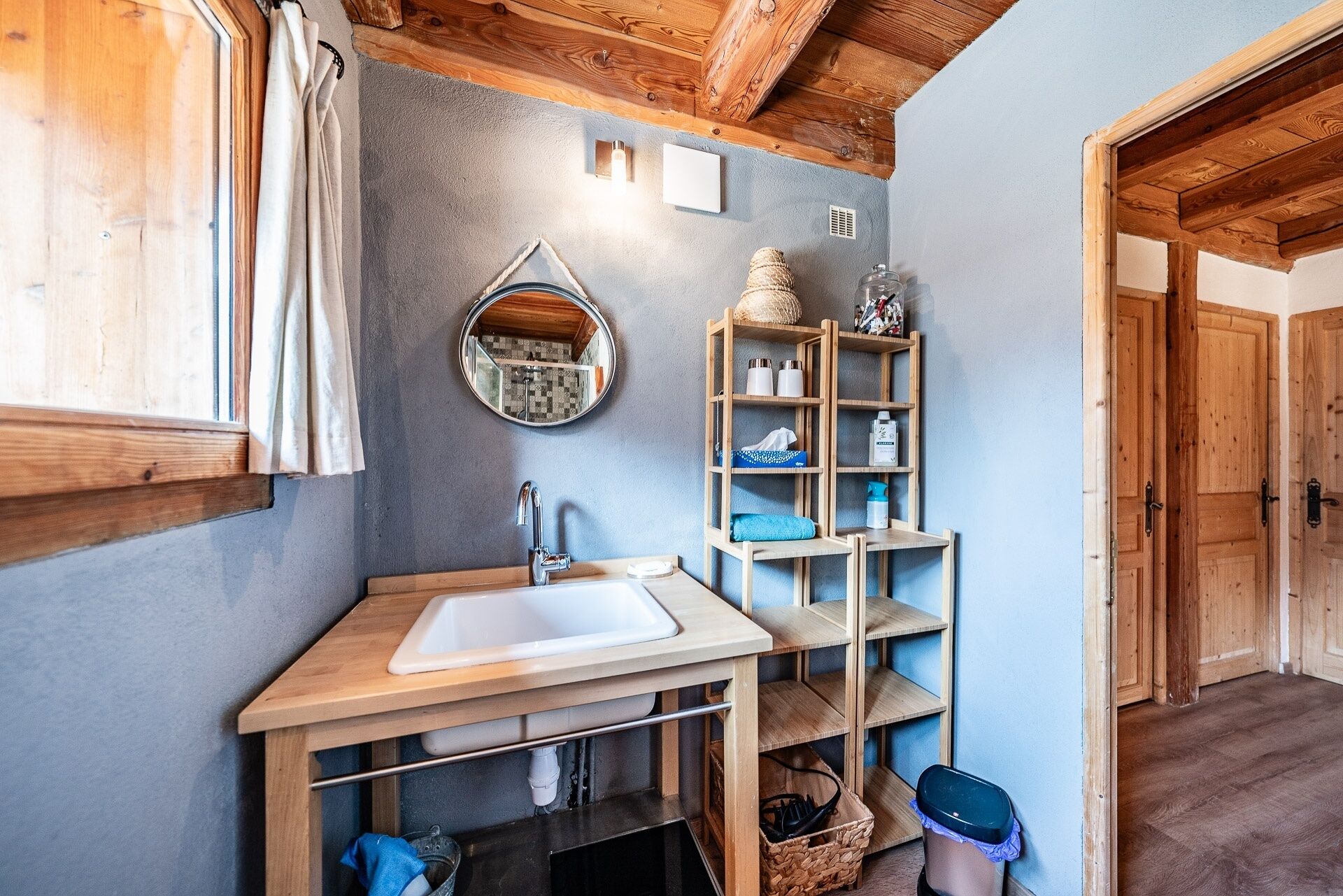 A bathroom with a wooden vanity, a sink, a mirror, and a shelf with toiletries.