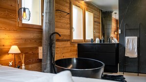 Moderni kylpyhuone, jossa on puuseinä, musta kylpyamme, pesuallas, jossa on hygieniatuotteita, ja pyyhekoukku.