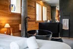 A modern bathroom with a wooden wall, a black bathtub, a sink with toiletries, and a towel rack. - Orezza - Four Bedroom Chalet, Sleeps 10 (La Salle-les-Alpes)