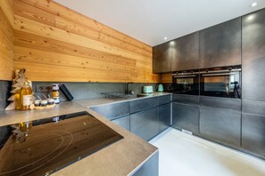 A modern kitchen with wooden paneling, a built-in oven, and a stainless steel backsplash. - Orezza - Four Bedroom Chalet, Sleeps 10 (La Salle-les-Alpes)
