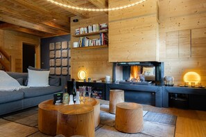 Ein gemütliches Holzblockhaus-Interieur mit Kamin, Bücherregalen, einer Couch und Holzschemeln.