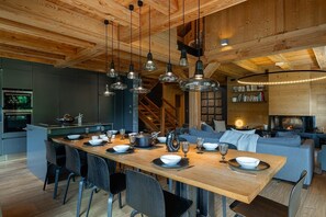 Eine moderne Küche mit Holzbalkendecke, ein Essbereich mit großem Tisch und einer eingebauten Bücherwand.