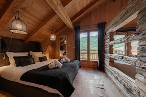 Ein Schlafzimmer in einer Blockhütte mit einem großen Bett, zwei Nachttischen, einer Pendelleuchte und Blick auf die Berge.
