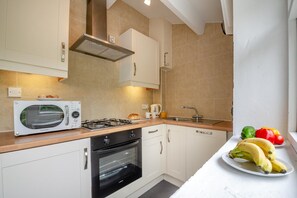 A kitchen with a microwave, stove, oven, and sink. There are bananas and vegetables on the counter. - 2 Bed in Betws Garmon (oc-b45268) (Betws Garmon)