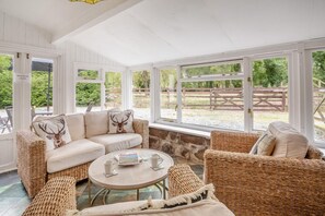 A cozy room with a sofa and chairs, a round table with a book and a cup, and large windows with a view of a fenced outdoor area. - 2 Bed in Betws Garmon (oc-b45268) (Betws Garmon)