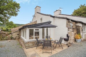 A stone house with a patio, outdoor seating, and a barbecue. - 2 Bed in Betws Garmon (oc-b45268) (Betws Garmon)