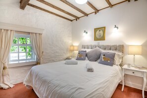 Ein Schlafzimmer mit einem großen Bett, zwei Nachttischen, einem Fenster mit Vorhängen und einem Wandbild.