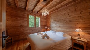A wooden cabin bedroom with a bed, two windows, a nightstand, and a hanging light fixture. - Trancoulette - Five Bedroom Chalet, Sleeps 12 (La Salle-les-Alpes)