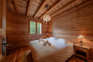Ein Schlafzimmer einer Holzhütte mit einem Bett, zwei Fenstern, einem Nachttisch und einer Pendelleuchte.