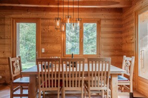 Ein Holzhütten-Interieur mit Esstisch, Stühlen und einer Hängeleuchte.