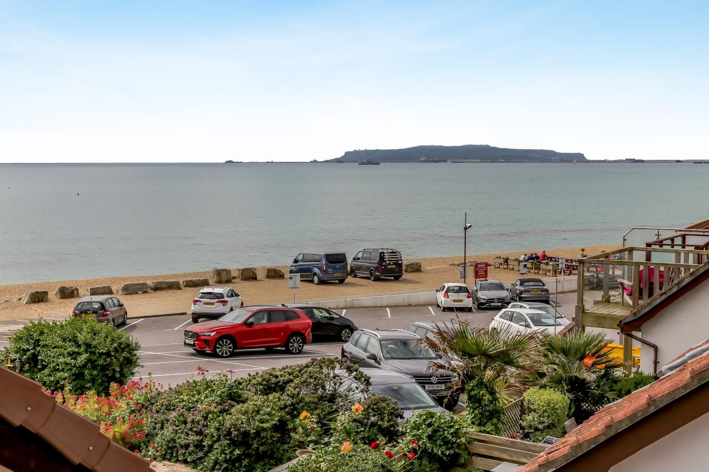 Ein Küstenparkplatz mit Fahrzeugen, einem Strand und einer entfernten Hügelkette.