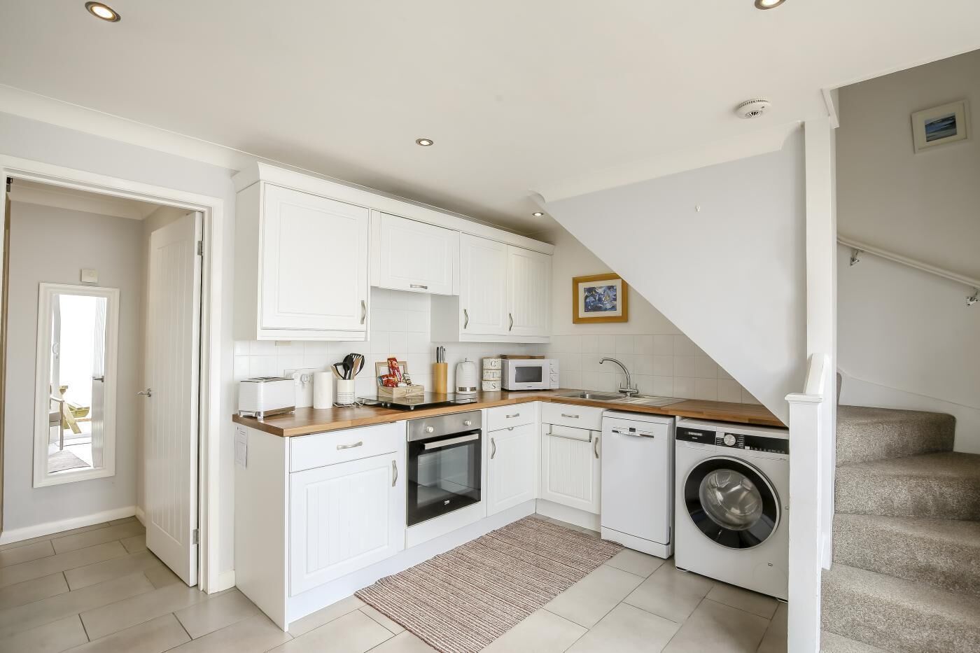 A compact kitchen with white cabinets, a microwave, a sink, and a washing machine.