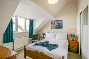 A bedroom with a bed, a chair, a nightstand, a lamp, a painting, and a window with curtains. - 2 Bed in Weymouth (oc-s42796) (Weymouth)