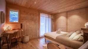 Una camera accogliente con soffitto in legno, un letto con cuscini, una scrivania con lampada, una sedia e un appendiabiti in macramè sulla parete.