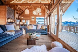Ein gemütliches Holzinterieur mit einer Couch, einem Couchtisch und großen Fenstern mit Blick auf die Berge.