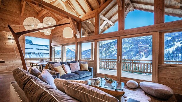 Un interno in legno con un divano, un tavolo e ampie finestre con vista sulle montagne.