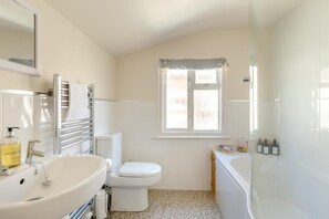 Un baño con lavamanos blanco, inodoro y bañera. Hay una ventana con un adorno a rayas y artículos de aseo visibles en la encimera.