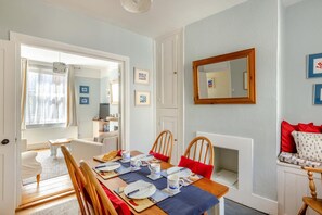 A dining area with a table set for four, chairs, a mirror, and a sofa with red cushions.