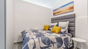 A bedroom with a bed, a nightstand, a painting on the wall, and a window.