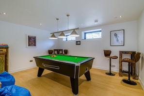 Une table de billard avec des billes, un tabouret de bar, une chaise et un tableau encadré au mur.