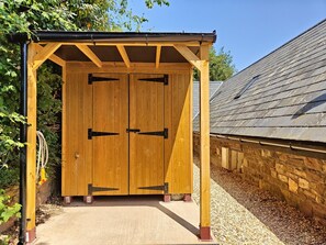 A wooden structure with a roof, two doors, and a gravel path leading to it.