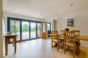 Un coin repas avec une table et des chaises en bois, une vue sur l’extérieur à travers des portes vitrées et un tableau encadré au mur.