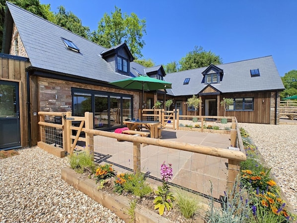 Un bâtiment moderne avec une façade en pierre, une terrasse en bois et un espace extérieur aménagé pour s’asseoir.