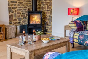 A cozy living room with a stone wall, a fireplace, a wooden coffee table, a colorful sofa, and a lamp.