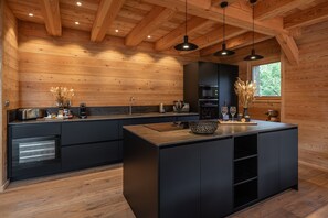 A modern kitchen with wooden walls, black cabinetry, and pendant lighting.