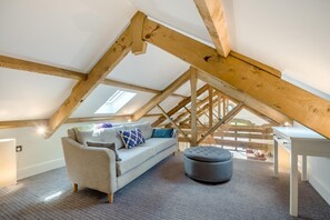 Ein Schlafzimmer im Loft-Stil mit geneigter Decke, einer Couch, einem Hocker und einem kleinen Tisch.
