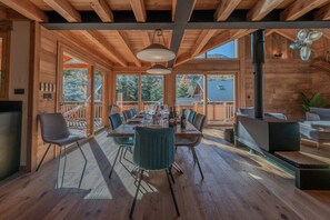 A wooden interior with a dining area, large windows, and a fireplace.
