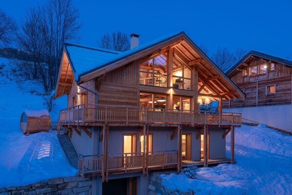 A wooden chalet with a balcony, stone foundation, and multiple windows.