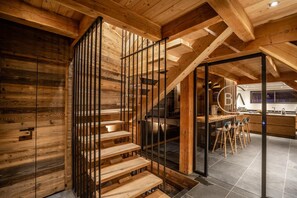 Una escalera de madera con un vidrio que da a una zona de cocina con taburetes de bar.