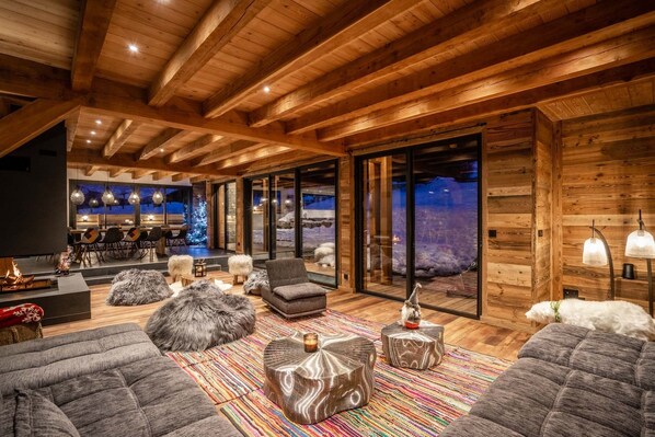 Una sala de estar acogedora con chimenea, asientos cómodos y un ventanal con vistas al paisaje nevado.