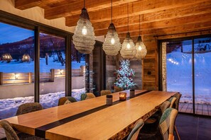 A dining area with a wooden table and chairs, hanging pendant lights, and a Christmas tree. - Beleza - Seven Bedroom House, Sleeps 15 (La Salle-les-Alpes)