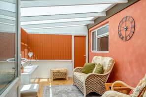 Ein Zimmer mit einem Korbstuhl, einem kleinen Tisch und einer Wanduhr.
