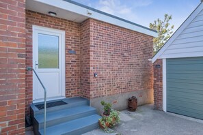 Ein Ziegelhaus mit einer weißen Tür, ein paar Stufen, die zu einer Garage führen, und einer grünen Garagentür.