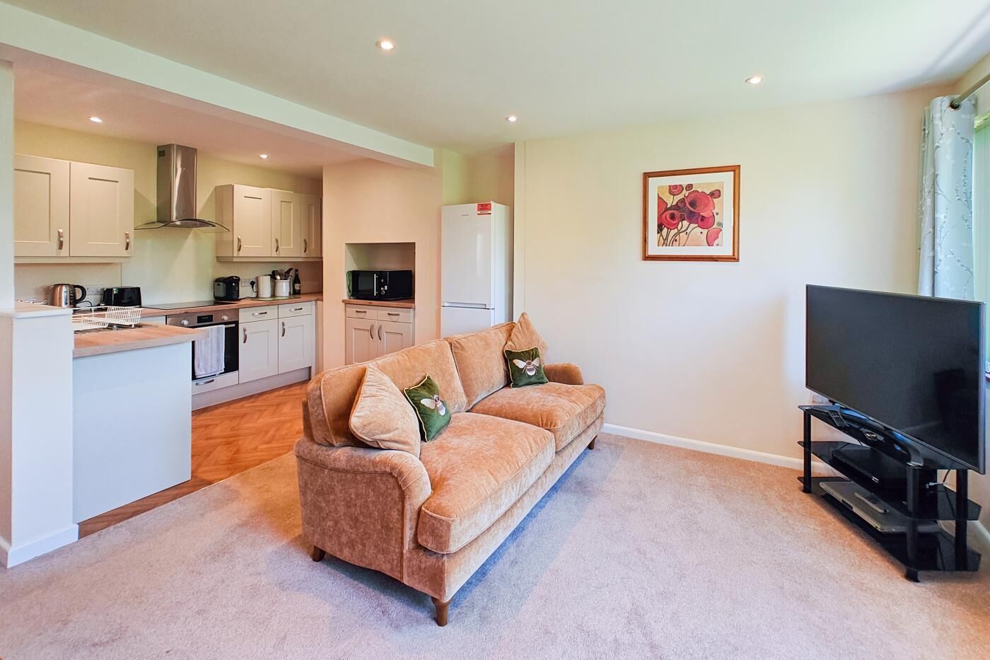 A living room with a sofa, a television, and a kitchen area in the background.