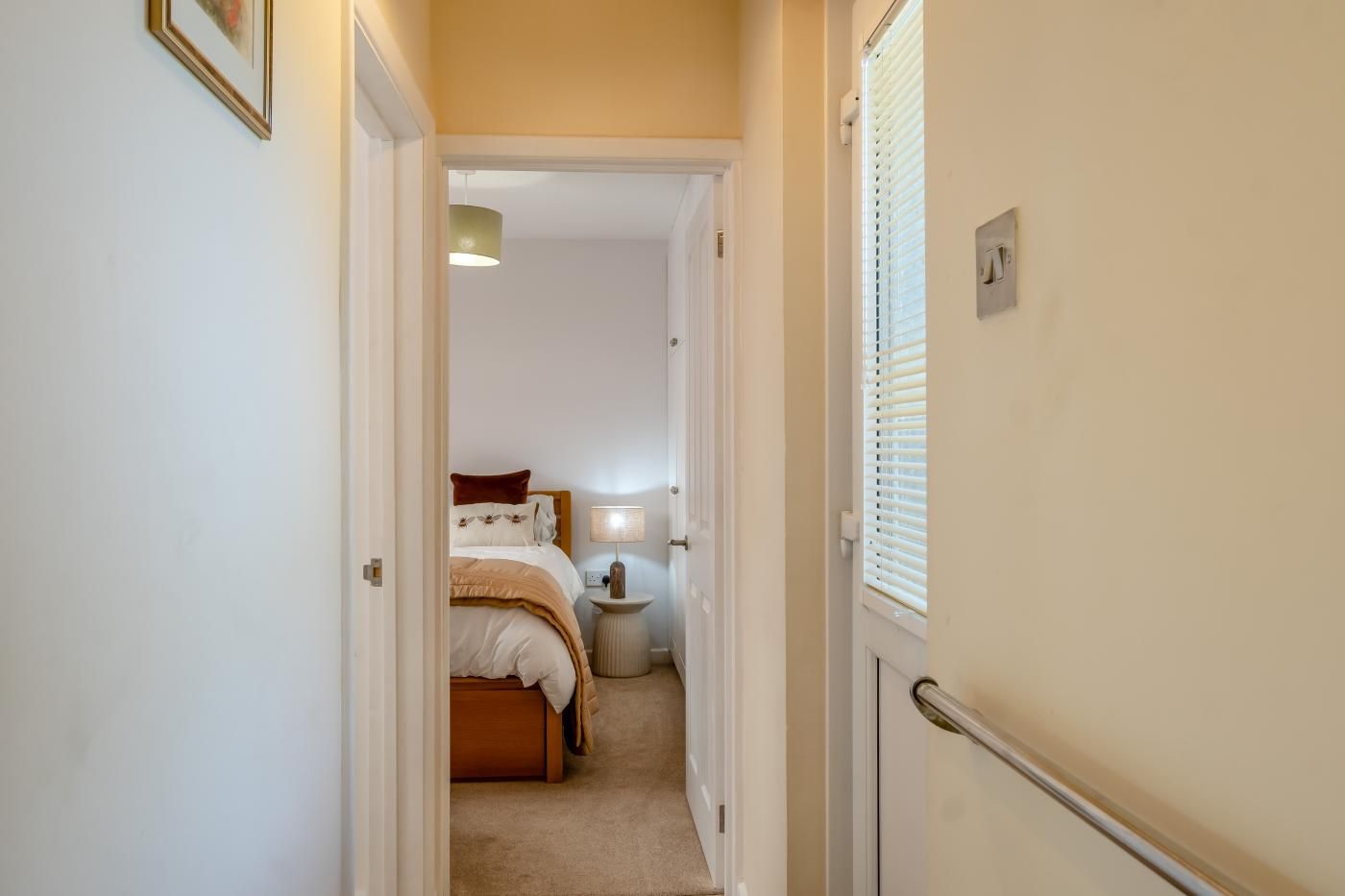 Un couloir étroit mène à une chambre à coucher qui contient un lit, une table de chevet et une lampe.