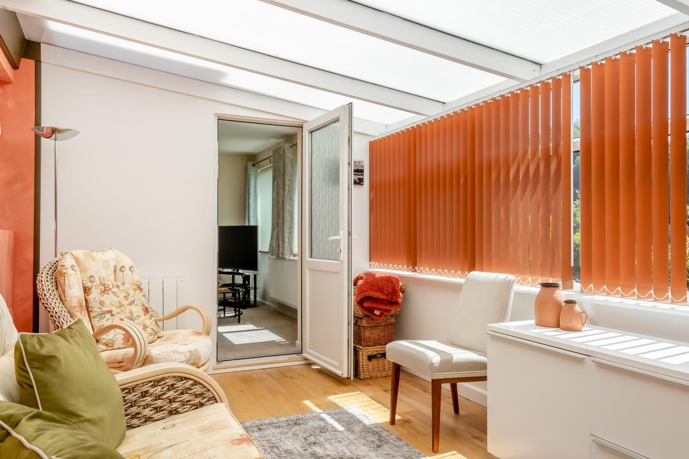 Un salon moderne avec un canapé, un fauteuil, un téléviseur et une fenêtre équipée de stores.