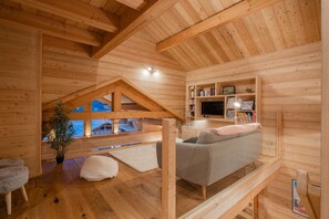 A cozy wooden cabin interior with a loft bedroom, a sofa, a TV, and a bookshelf. - Aigle - Six Bedroom House, Sleeps 14 (Le Monêtier-les-Bains)