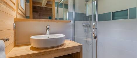 A bathroom with a wooden vanity, a white sink, and a glass shower enclosure.