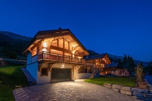 A two-story wooden house with a balcony, stone driveway, and a garage. - Aigle - Six Bedroom House, Sleeps 14 (Le Monêtier-les-Bains)