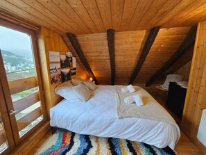 Ein Schlafzimmer einer Holzhütte mit einem Bett, Kissen, einer Decke, einem Teppich und Blick durch ein Fenster.