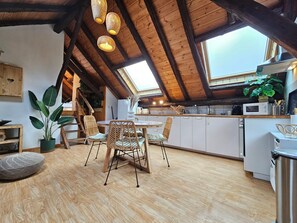 Eine gemütliche Küche mit Holzbalken, eine Essecke mit Korbstühlen und ein großes Fenster.