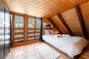 A bedroom with a wooden ceiling, a bed, a nightstand, and a window with a view of a mountain. - Acolin - One Bedroom Apartment, Sleeps 6 (Briancon)