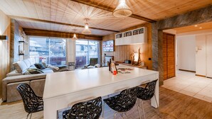A modern interior with a wooden ceiling, a central island with bar stools, a sofa, and a TV mounted on the wall. - Europa - Three Bedroom Apartment, Sleeps 8 (Briancon)